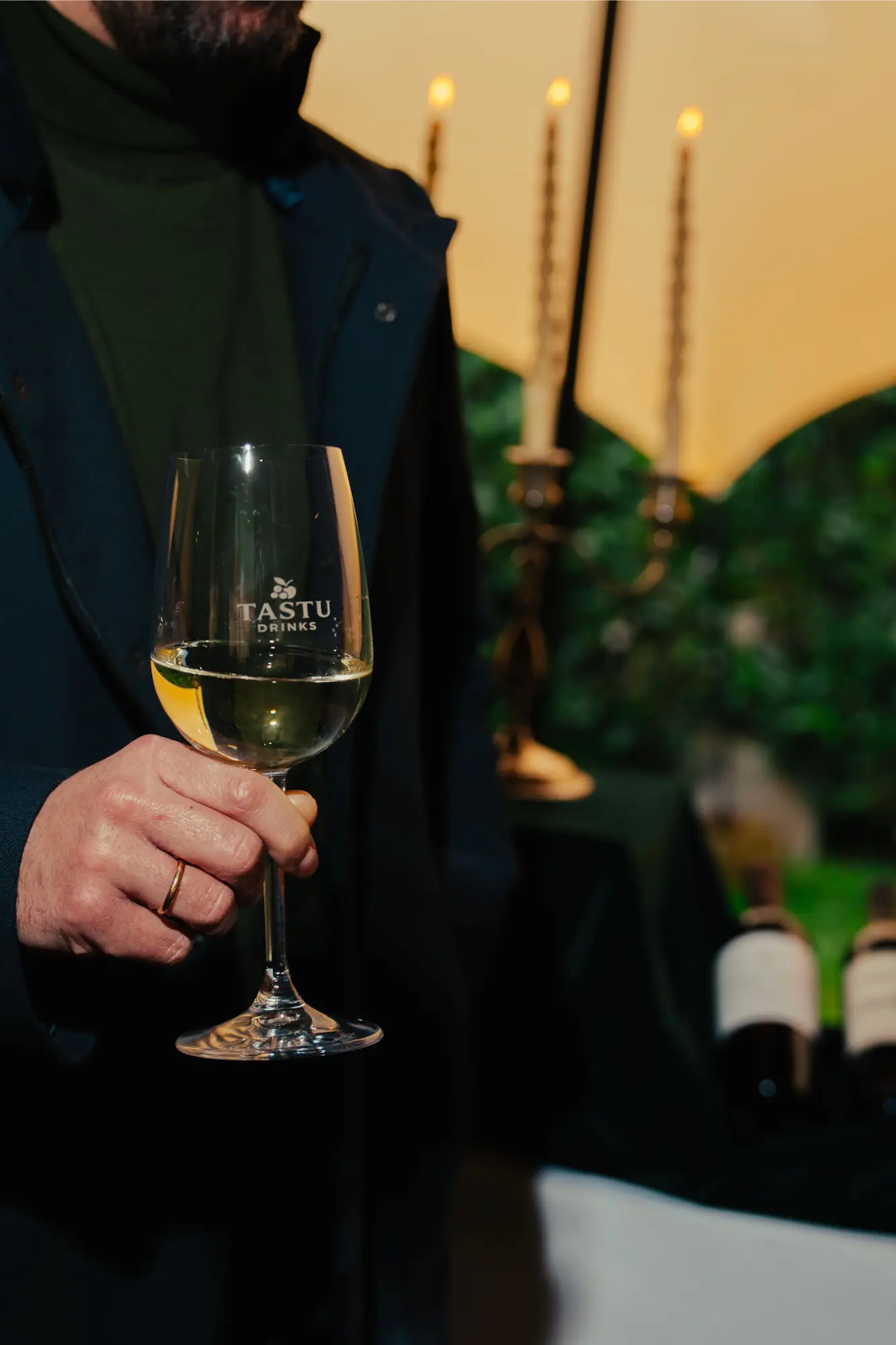 Hombre elegante con americana sosteniendo una copa de vino blanco con el logo de Tastu.
