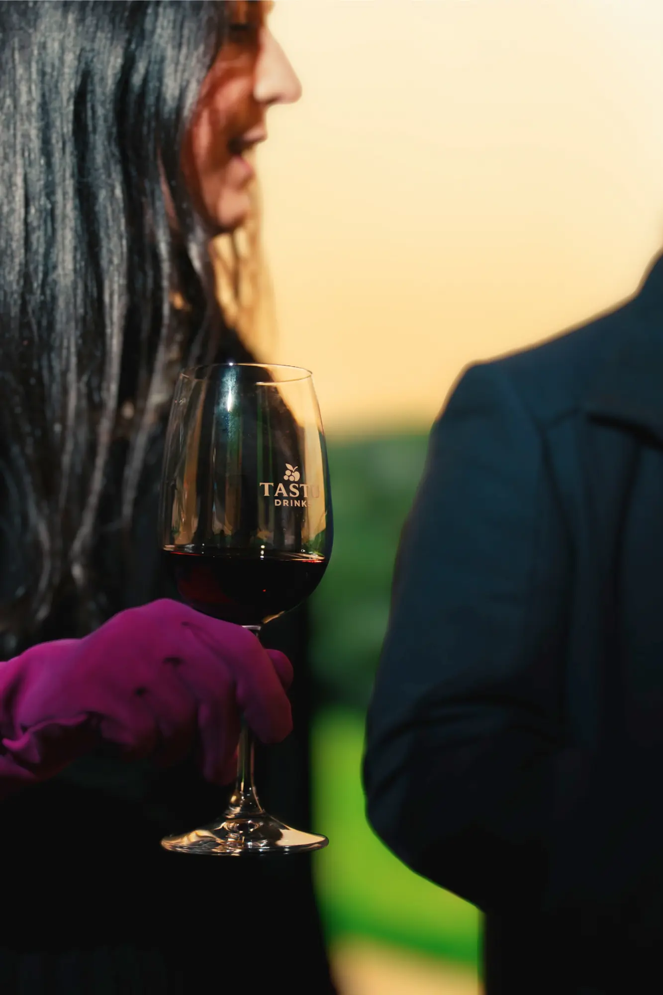 Mujer con guante fucsia sosteniendo una copa de vino tinto con logo de TASTU DRINK.