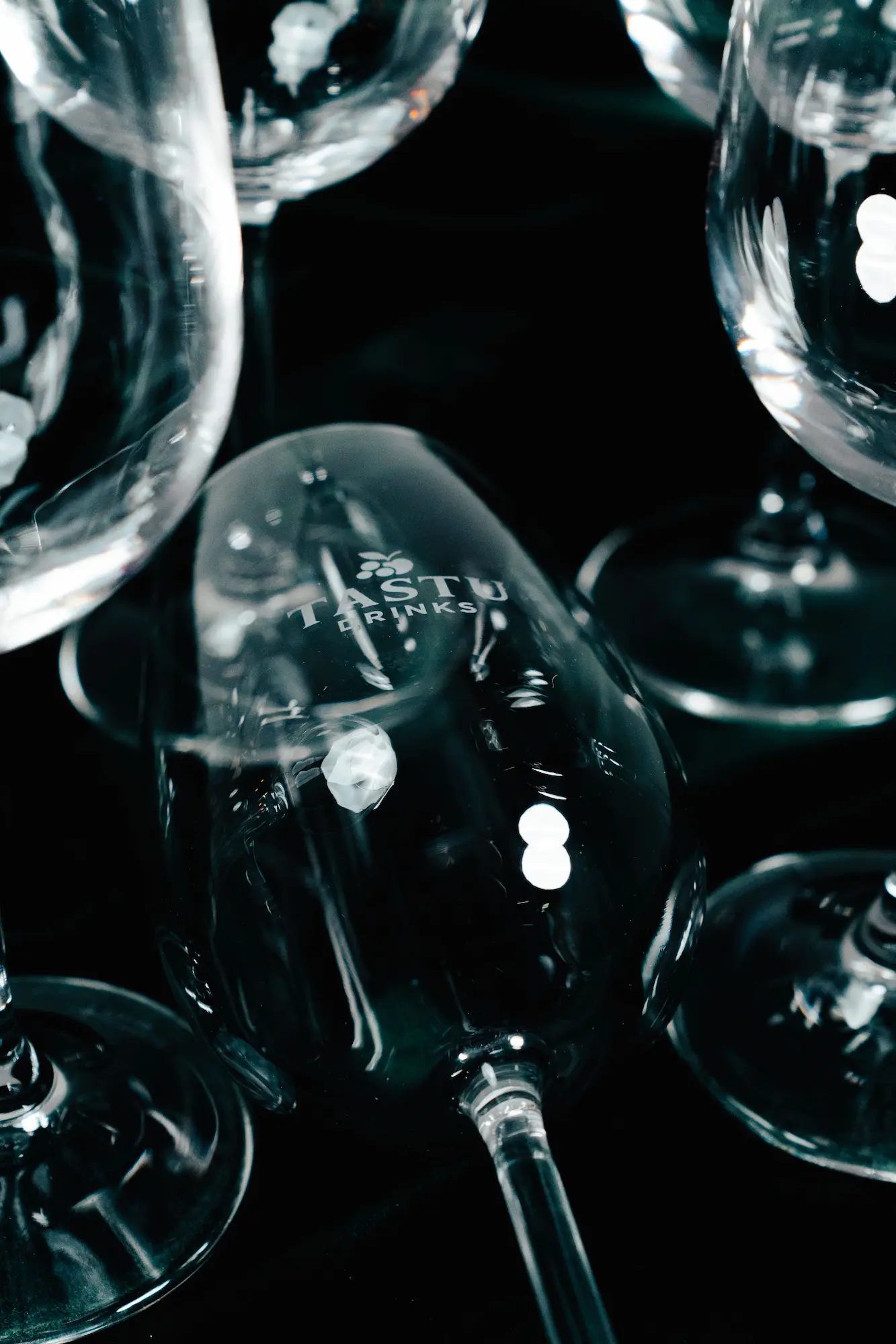 Dos copas de cristal vacías con el logo Tastu Drink enfrentadas sobre un fondo negro sólido.