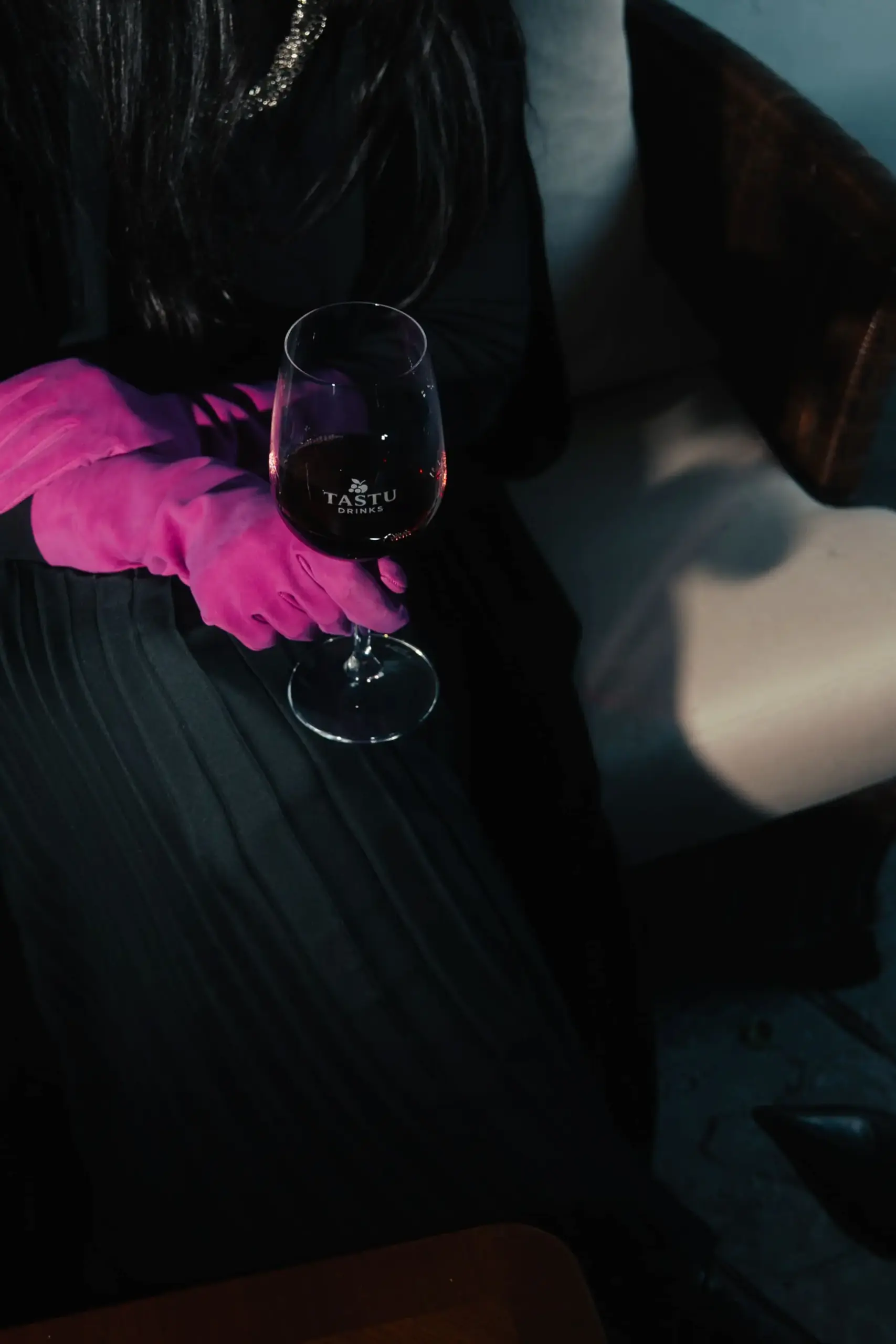 Tastu Drinks - Estaciones de Vino y Sidra Persona con vestido negro y guantes fucsia sosteniendo copa de vino tinto Tastu Drink en ambiente nocturno.